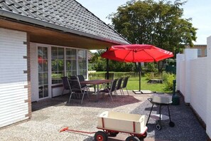 Eine Terrasse mit Tisch und Stühlen, einem roten Sonnenschirm, einem Grill und einem Schubkarren.