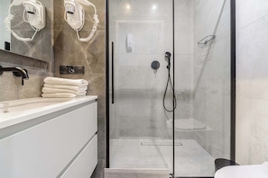 Ein modernes Badezimmer mit einer gläsernen Duschkabine, einem Waschtisch mit Handtuchhalter und einem an der Wand befestigten Föhn.