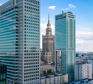 Eine Stadtansicht mit modernen Hochhäusern, einem historischen Turm und blauem Himmel.