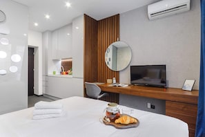 Ein modernes Hotelzimmer mit einem Bett, einem Schreibtisch mit Fernseher, einem Spiegel und einer Wandklimaanlage.