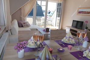Ein Zimmer mit einem Bett, einem Esstisch für zwei Personen, einem Fernseher und einem Balkon mit Stühlen.