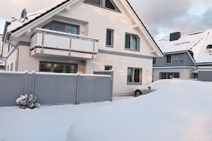 Ein zweistöckiges Haus mit Balkon, Garage und einer verschneiten Auffahrt.