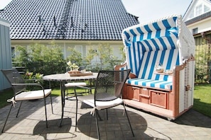 Eine Terrasse im Freien mit einem runden Tisch, zwei Stühlen und einer gestreiften Liege.