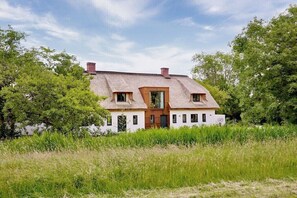Ein Haus mit einem Strohdach, umgeben von hohem Gras und Bäumen.