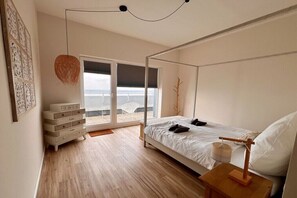 Un dormitorio con cama con dosel, una mesita de noche con lámpara, un aparador y vistas al exterior a través de una puerta corredera.