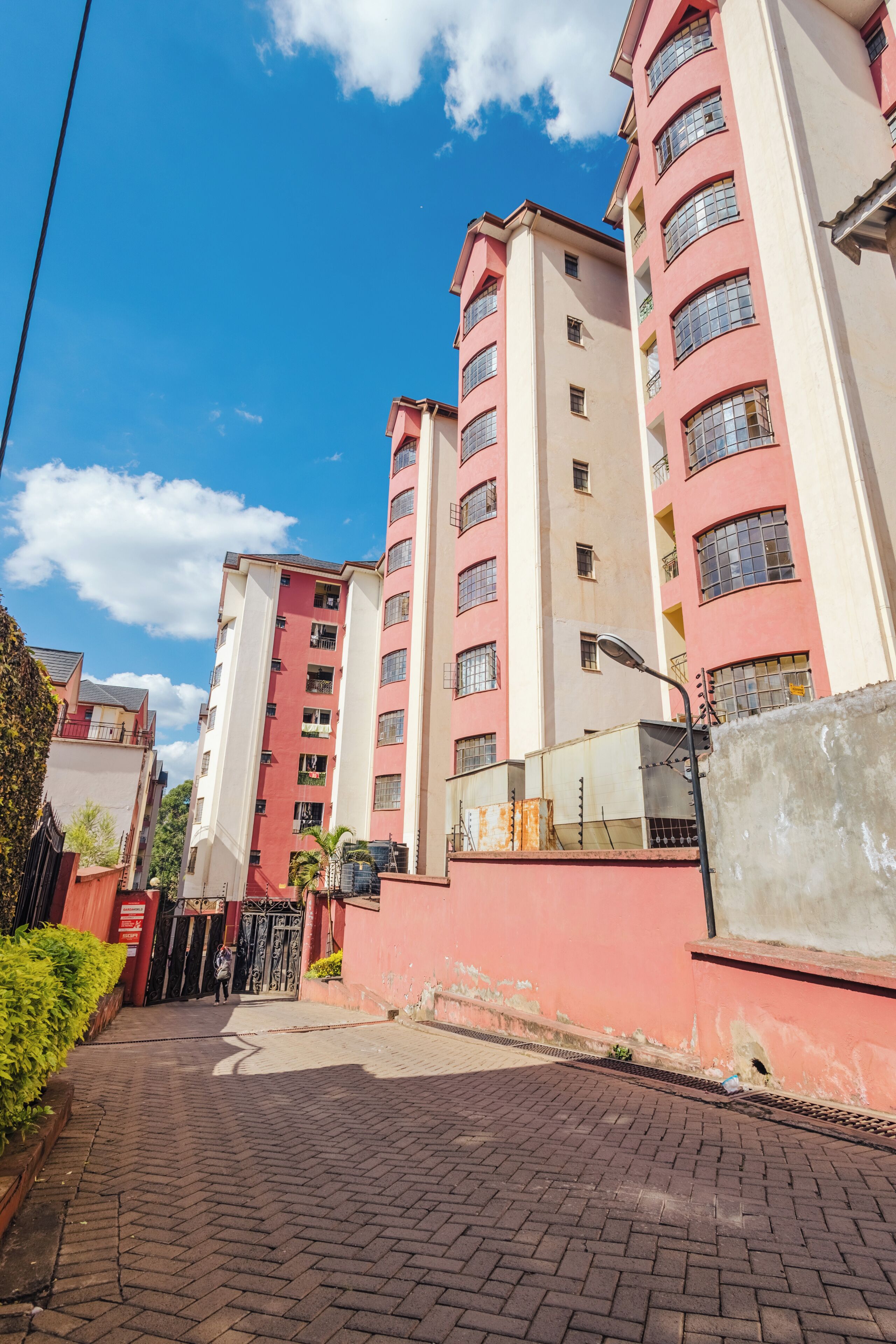 A multi-story residential building with a red and white facade, a paved entrance, and a clear blue sky.