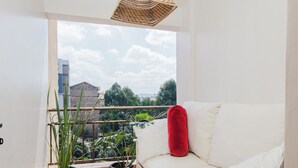 Un balcone con una divisa bianca, un cuscino rosso, piante in vaso e un lampadario in rattan.