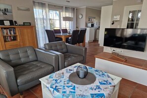 Ein Wohnzimmer mit einer Couch, einem Couchtisch mit gemustertem Tischläufer, einem Flachbildfernseher und einem Essbereich mit Stühlen und einem Tisch.