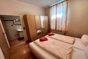 Ein Hotelzimmer mit zwei Betten, einem Holzschrank, einem Spiegel, einem Waschbecken und einem Fenster mit Vorhängen.