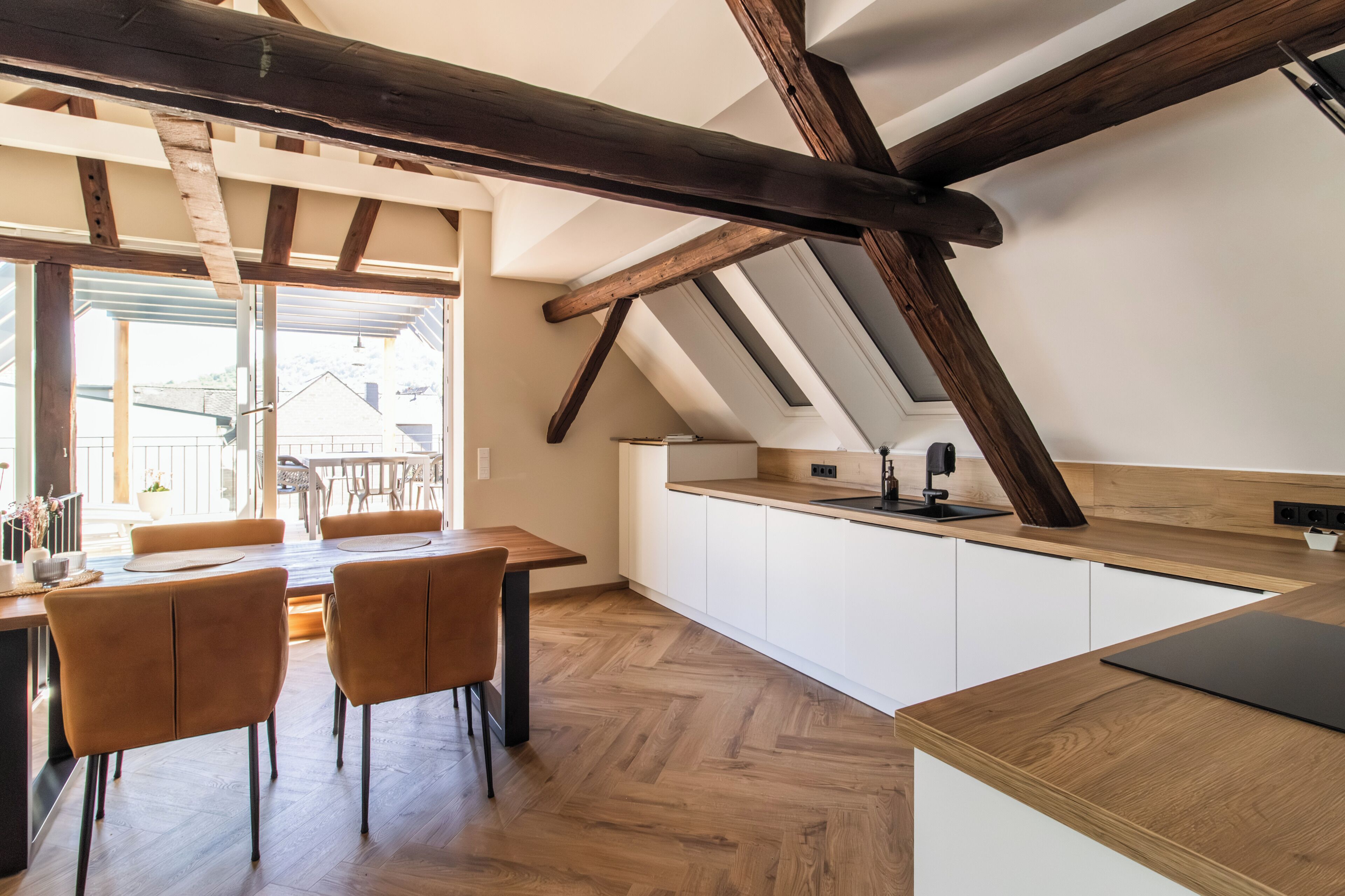 Eine moderne Küche mit Holzbalken, weißen Schränken und einem Essbereich mit Stühlen.