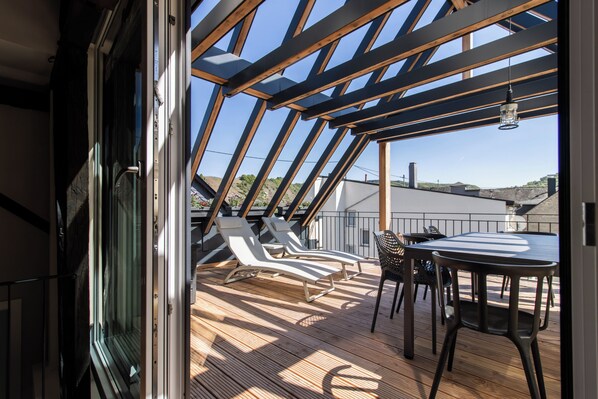 A wooden deck with two lounge chairs and a table, a glass door leading to an outdoor area, and a clear sky. - Modern, spacious vacation apartment with panoramic Moselle terrace (Bremm)