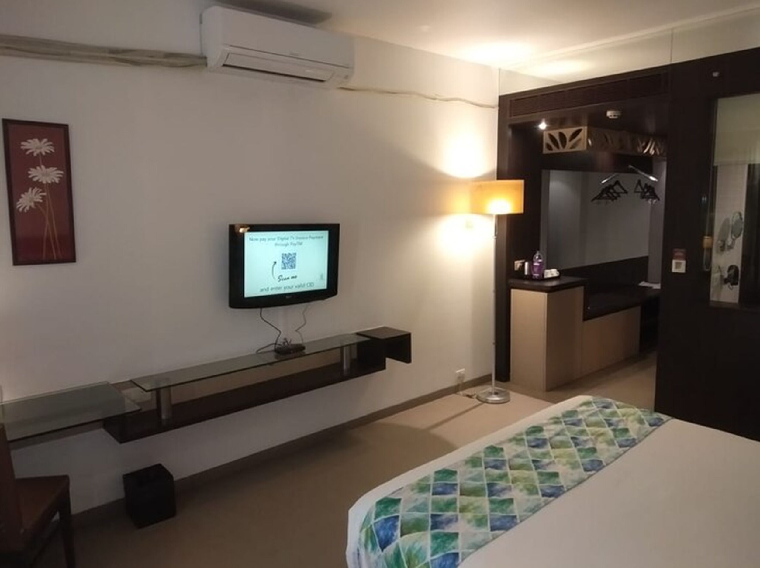 Habitación de hotel con cama, televisor montado en la pared, una mesita y un espejo.