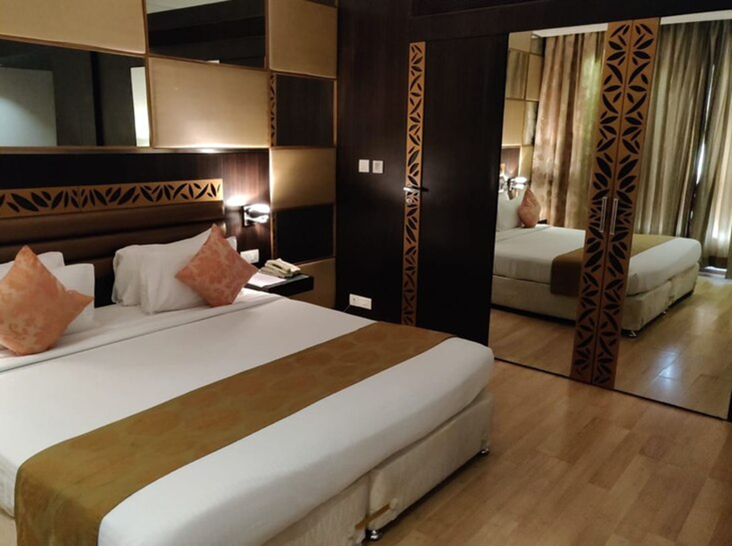 Ein Hotelzimmer mit einem großen Bett, einem Nachttisch, einem Spiegel und Blick auf ein weiteres Zimmer.