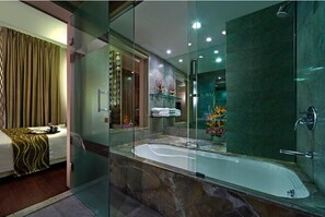Ein modernes Hotelzimmer mit einem von Glas umschlossenen Badezimmer, das eine Badewanne, eine Dusche und eine Glastrennwand beinhaltet.