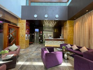 A hotel lobby with a reception desk, purple sofas, a glass coffee table, and a marble floor. - Hotel Supreme Heritage (Pune)
