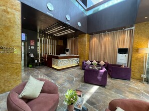 Eine Lobby mit einer Rezeption, violetten Sofas, einem Couchtisch, einer Pflanze und einer Wanduhr.