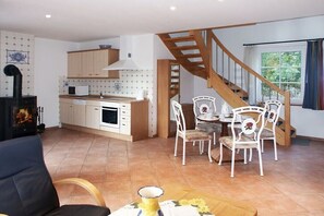 A kitchen with a stove, cabinets, and a dining area with chairs and a table. - Rose House in Heide Park (Nebel\/Süddorf)
