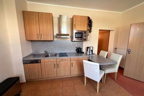 A compact kitchen with wooden cabinets, a microwave, a sink, and a dining area with a table and chairs. - House Andrea Apartment 1 (Norderney)