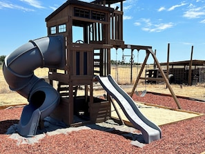Une aire de jeux avec un toboggan, une balançoire et une structure en forme de maisonnette.