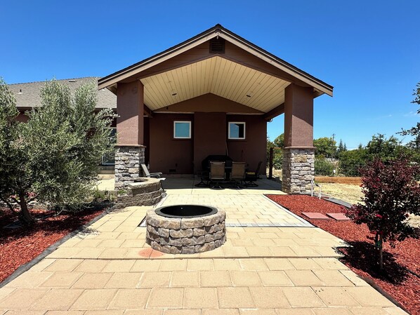 A house with a covered patio, stone pillars, a fire pit, and outdoor furniture.