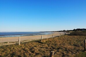 A beach with a wooden fence, grassy dunes, and a clear blue sky.