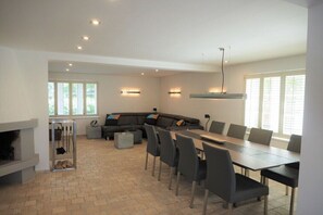 A spacious living area with a fireplace, a large sofa, a dining table with chairs, and a kitchen area.