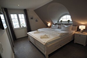 Ein Schlafzimmer mit einem großen Bett, zwei Nachttischen, einem Fenster und einer geneigten Decke.