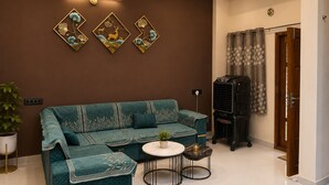A living room with a teal sofa, a small round table, a potted plant, and a black heater. - Shivansh Stays (Ujjain)