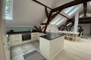 Eine moderne Küche mit einer zentralen Kochinsel, einem Essbereich mit Tisch und Stühlen sowie einer geneigten Decke mit Dachfenstern.