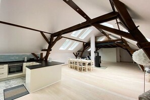 Ein geräumiges Loft mit hohen Decken, Dachfenstern, einer Küchenzeile und einem Esstisch.