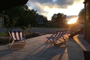 Zwei gestreifte Lounge-Sessel auf einer gepflasterten Terrasse mit Sonnenuntergang im Hintergrund.