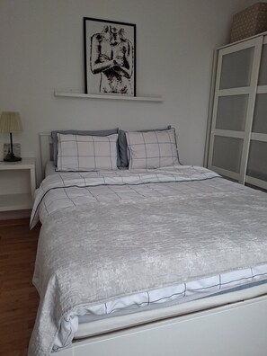A bedroom with a bed, a nightstand, a lamp, a framed artwork, and a wardrobe.