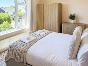 A bedroom with a bed, a window, a wardrobe, and a bedside table with a plant. - 2 bedroom accommodation in Porthleven (Porthleven)