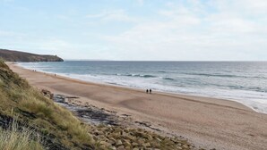 Une plage côtière avec un premier plan rocheux, une rive sablonneuse et un ciel dégagé.