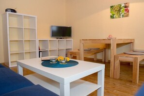 Ein Wohnzimmer mit einem weißen Tisch, einem Fernseher, einem Bücherregal und einem Etagenbett.