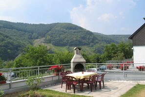 Eine Terrasse mit Kamin aus Stein, Sitzgelegenheiten und Blick auf einen bewaldeten Berg.