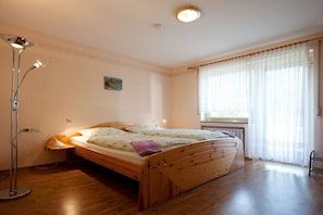 Ein Schlafzimmer mit einem hölzernen Bett, einer Stehlampe, einem Fenster mit durchsichtigen Vorhängen und einer Heizung.