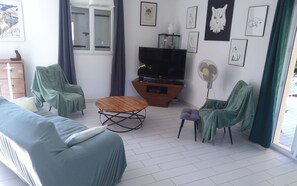Ein Wohnzimmer mit einer Couch, Sesseln, einem Couchtisch, einem Fernseher und Kunstwerken an den Wänden.