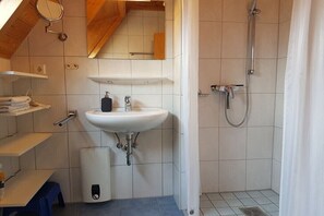 Et badeværelse med vask, spejl, bruser og fliserede vægge.