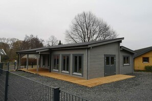 A modern two-story building with a covered patio area, large windows, and a gravel driveway.