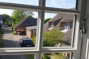 Blick durch ein Fenster auf eine Wohnstraße mit Häusern, einem parkenden Auto und einem Fahrrad.
