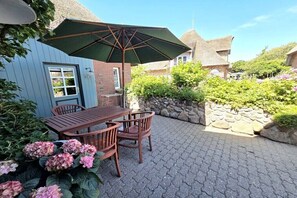 Eine Terrasse mit Tisch, Stühlen, einem grünen Sonnenschirm und einer Steinmauer.