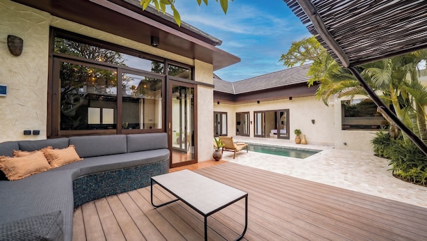A modern outdoor living area with a wooden deck, a gray sofa, and a pool. - Villa Frika Canggu (Canggu)