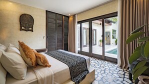 A bedroom with a bed, a patterned throw, a headboard, and a view of an outdoor area. - Villa Frika Canggu (Canggu)