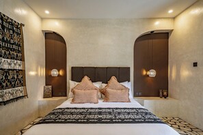 Een hotelkamer met een bed, twee sierkussens, een wandlamp en een kamerbreed tapijt met een patroon.