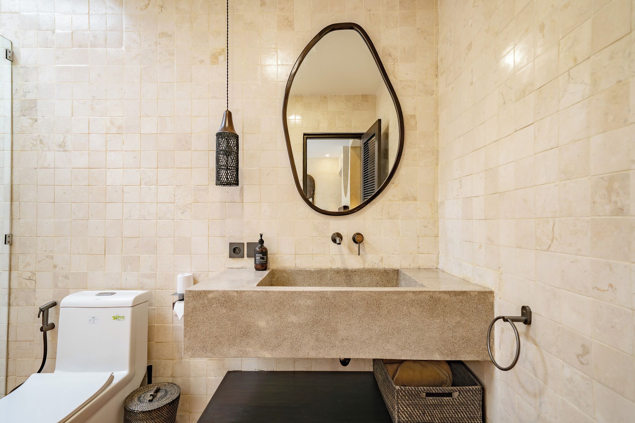 A bathroom with a beige tiled wall, a rectangular sink with a mirror above it, a towel rack, and a toilet.