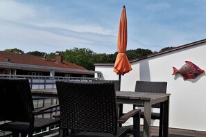 Eine Terrassengaststätte mit Korbmöbeln, einem orangefarbenen Sonnenschirm und einem dekorativen Fisch an der Wand.