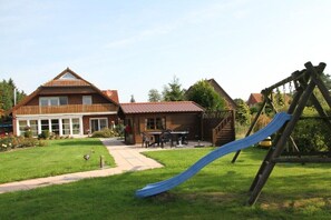 Ein Wohnhaus mit großem Garten, einer Holz-Spielanlage und gepflegtem Rasen.