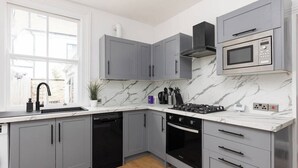 A modern kitchen with grey cabinets, a built-in microwave, and a stove. - New! Modern 2BR House w/ Patio in Acton (Greater London)