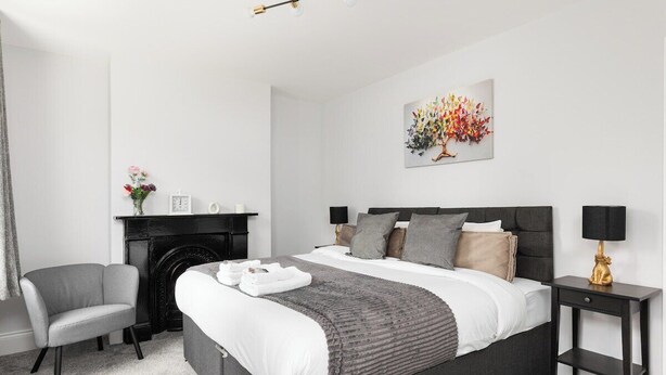 A modern bedroom with a bed, a chair, a fireplace, and a nightstand. - New! Modern 2BR House w/ Patio in Acton (Greater London)